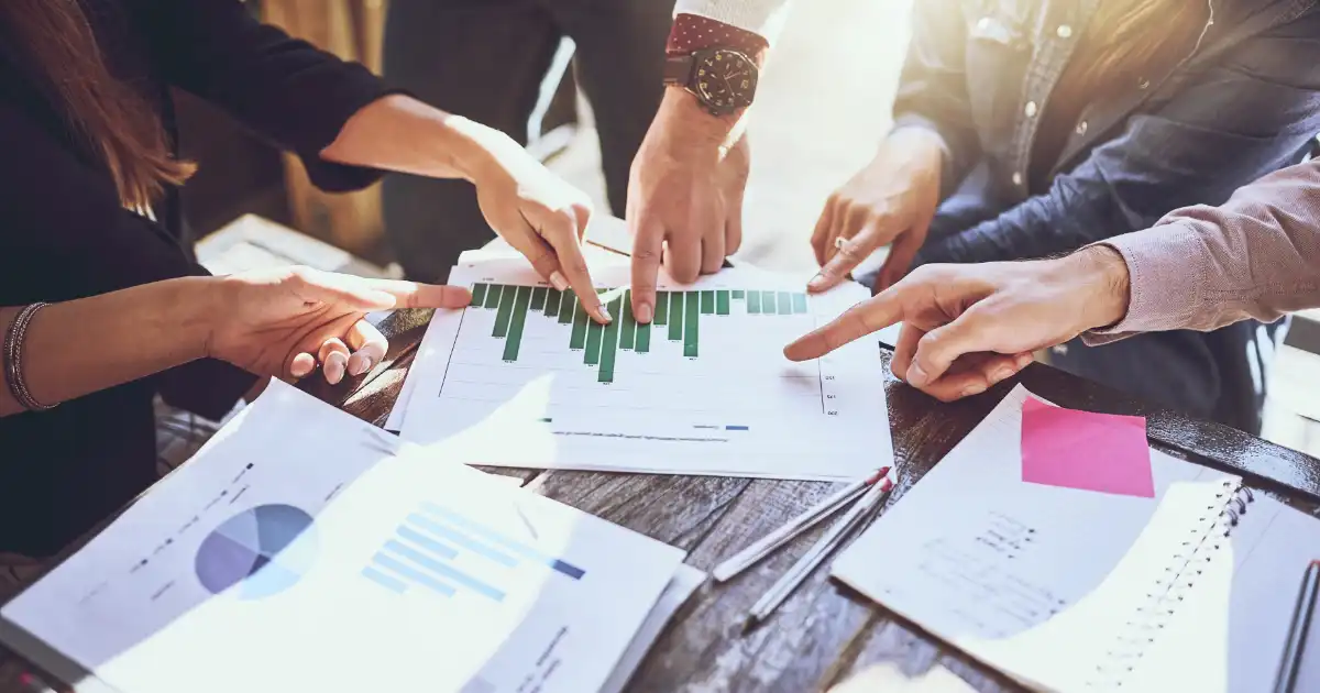 Team members pointing at printed financial charts during a business strategy meeting.